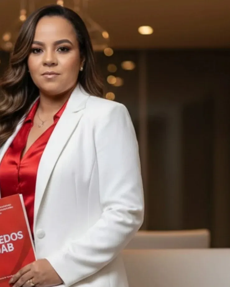 Professora Wanessa Matias sentada, de terno branco, com um livro nas mãos
